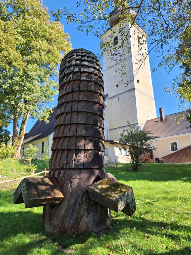 Vlevo Herz (Anne Knoll, dub, 1998), vpravo Bienenstock od Rumuna Dinu Campeanua (dub, 1998) pod věží farního kostela - Sochařský park Irdning - 18. 9. 2025 - Foto: Jiří Provazník