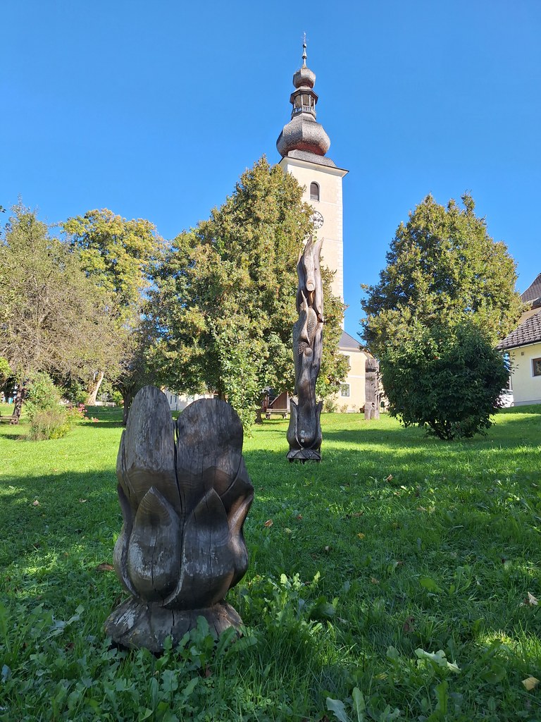 Dřevěný totem a poupě před věží farního kostela svatých Petra a Pavla - Sochařský park Irdning - 18. 9. 2025 - Foto: Jiří Provazník